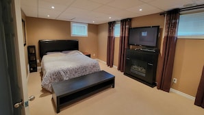 A bedroom with a bed, a TV, a fireplace, and a bench.