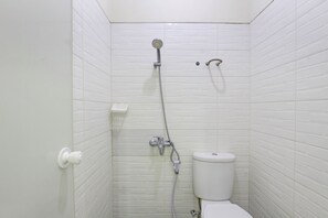 A small, white-walled bathroom with a toilet, a showerhead, and a faucet.