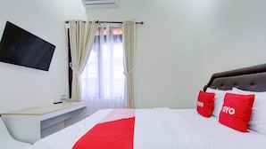 A hotel room with a bed, a desk, a TV, and curtains. - Hotel O Syariah Griya Wisata (Wonogiri)