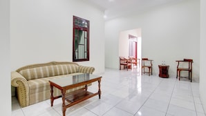 A living room with a sofa, a coffee table, and two wooden chairs. - Hotel O Syariah Griya Wisata (Wonogiri)