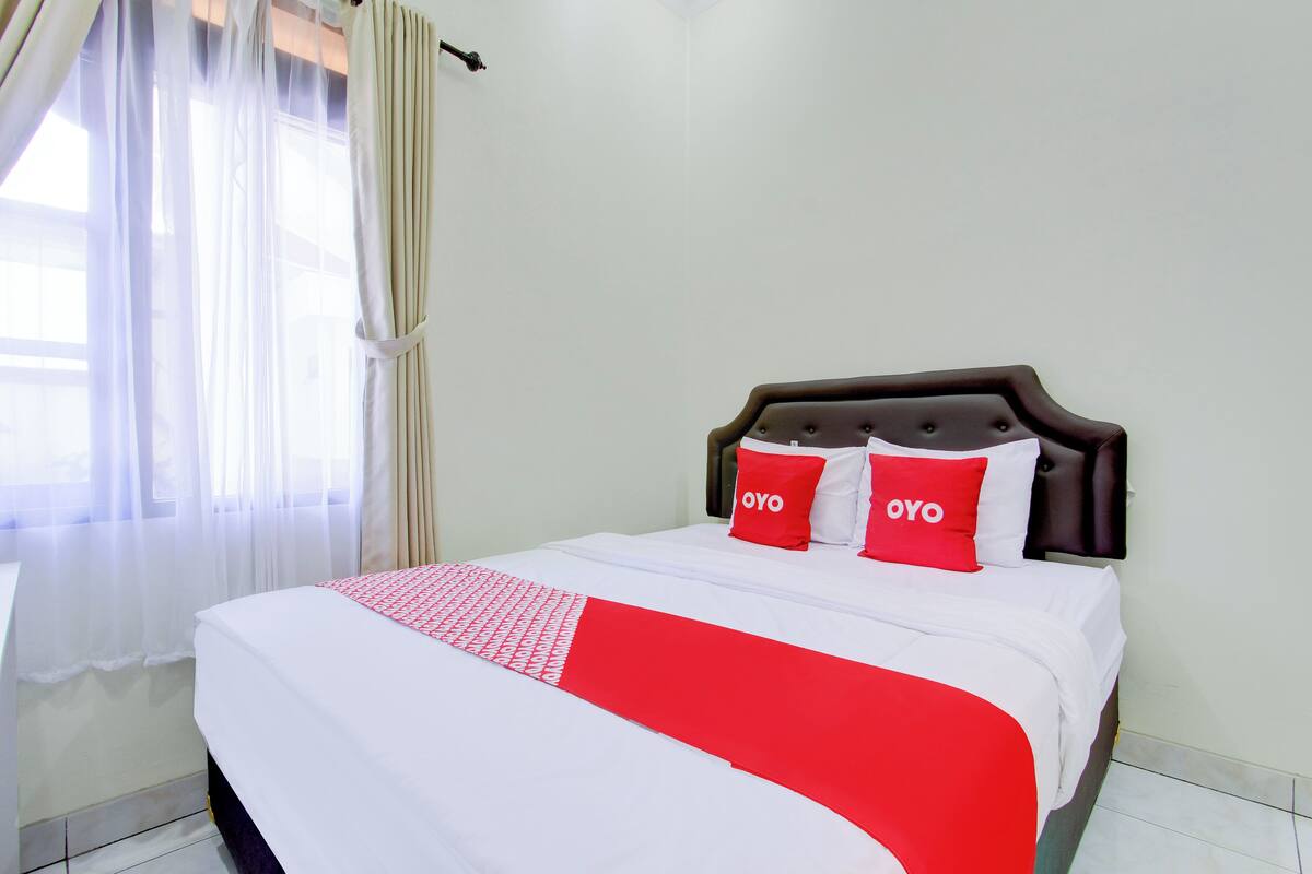 A neatly made bed with a white and red bedspread, two red pillows with "OYO" text, and a dark headboard.