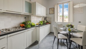 Uma cozinha moderna com armários brancos, bancada preta e área de refeições com mesa e cadeiras de vidro.