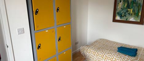 A room with a large yellow storage unit, a patterned bed, a blue towel, and a red chair.