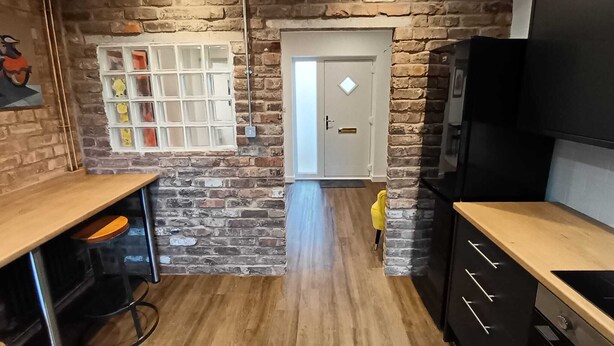 Une cuisine avec un mur en pierre, un plancher en bois et un réfrigérateur noir.