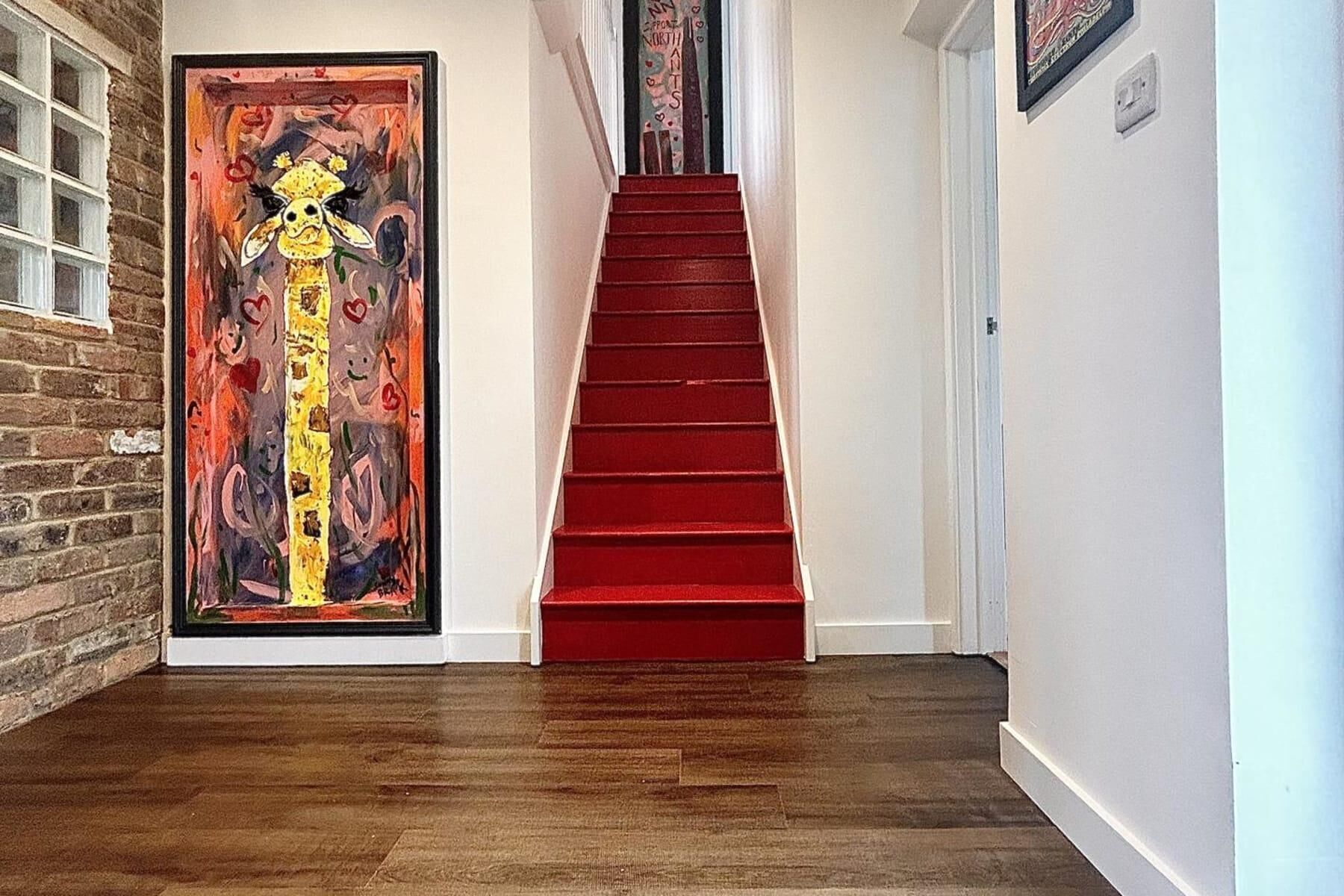 A staircase with red steps leading to a door with a colorful painting.