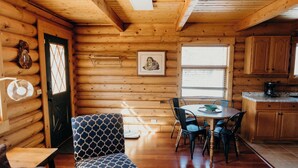 Ein gemütliches Blockhaus-Interieur mit Essbereich, einem gemusterten Sessel und einer Küche mit Holzschränken.
