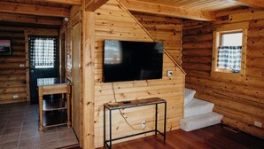 Ein Holzblockhaus-Innenraum mit an der Wand montiertem Fernseher, einem kleinen Tisch und einer Treppe.