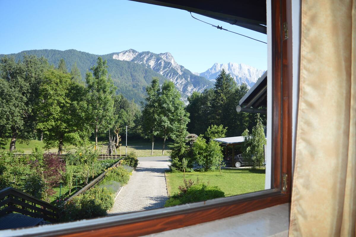 A view from a window overlooking a mountain landscape with a paved path leading to a building.