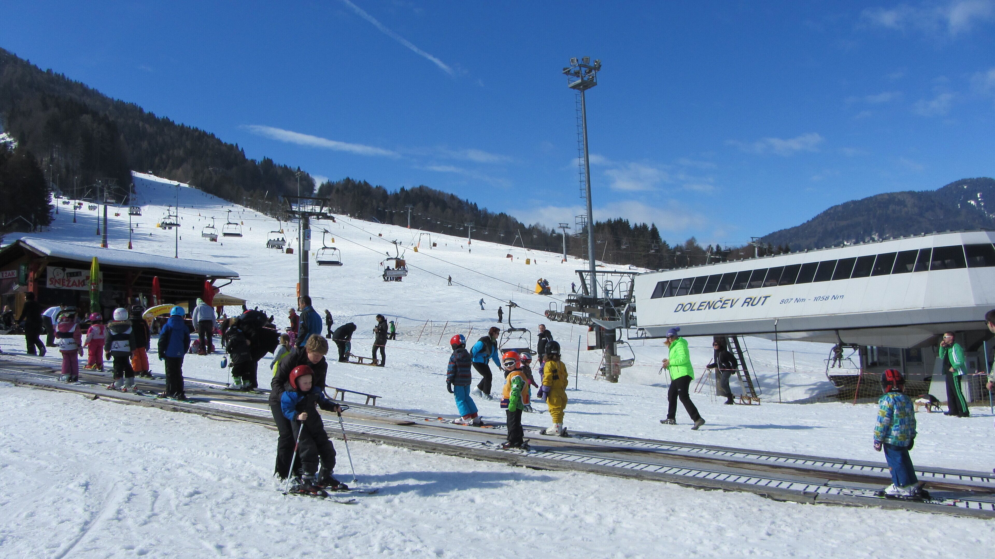 A ski resort with a ski lift, snow-covered slopes, and a mountain backdrop.