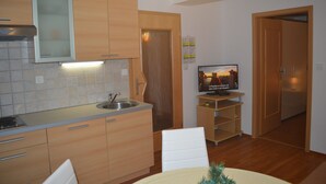 A compact kitchen with wooden cabinets, a built-in oven, and a small dining area with a table and chairs. - Apartments Jakelj (Kranjska Gora)