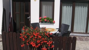 A patio with a wooden fence, a table, and chairs. There are windows with curtains and a door. - Apartments Jakelj (Kranjska Gora)