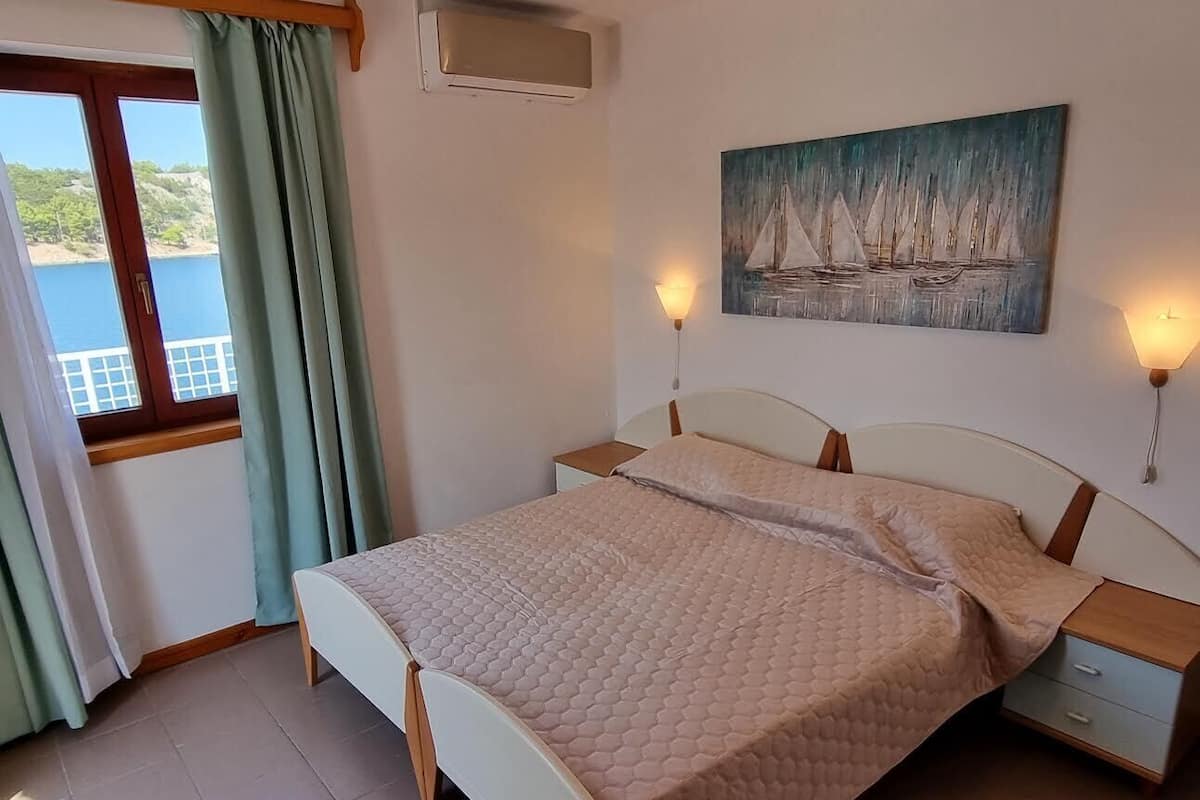 A bedroom with a bed, a window with curtains, a painting on the wall, and bedside lamps.