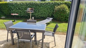 A patio with a table and chairs, a barbecue grill, and a hedge in the background. - Maison Dans Lotissement Très Calme 300 Mètres du Centre Ville .10 km de la mer (La Haye)