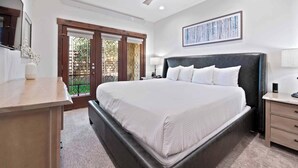 Une chambre avec un grand lit, un bureau, un ventilateur de plafond et une fenêtre donnant sur un paysage verdoyant.