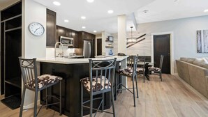 A modern kitchen with a central island, bar stools, a dining table, and a clock on the wall. - The Charter at Beaver Creek A2505 (Beaver Creek)