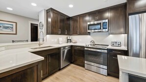 A modern kitchen with dark wood cabinets, stainless steel appliances, and a white countertop. - The Charter at Beaver Creek A2505 (Beaver Creek)