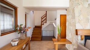 A modern interior with a wooden staircase, a stone wall, and a dining area with a table and chairs.