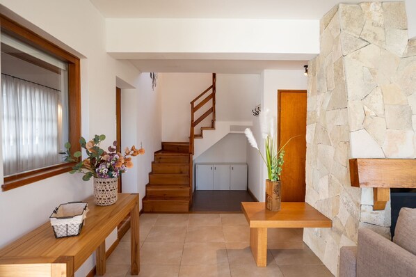 A modern interior with a wooden staircase, a stone wall, and a dining area with a table and chairs.