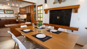 A dining area with a wooden table set for six, surrounded by white chairs.