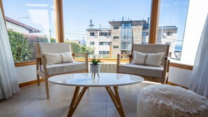A modern living room with two wooden chairs, a white round table, and a fluffy ottoman.