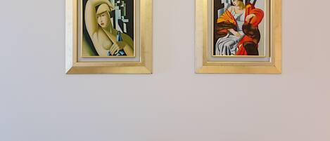Dos obras de arte enmarcadas en una pared, con dos sillas blancas al frente.