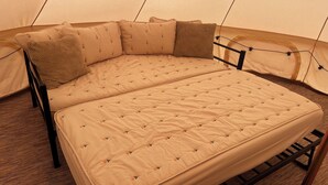 Une tente équipée d’un lit avec un matelas matelassé et des oreillers à motifs de feuilles.