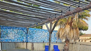 Una terraza de madera con piscina, sillas reclinables azules y una mesa con sillas.