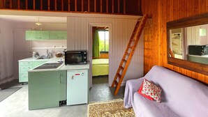 A compact kitchen with a refrigerator, microwave, and sink. A ladder is leaning against the wall, and a sofa with a cushion is in the foreground. - The cottage (Ploubazlanec)