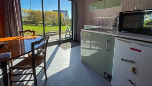 A modern kitchen with a large window, a dining table with chairs, and a microwave. - The cottage (Ploubazlanec)