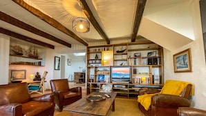 Een gezellige woonkamer met leren banken, een houten salontafel en een boekenplank vol boeken en decoratieve objecten.