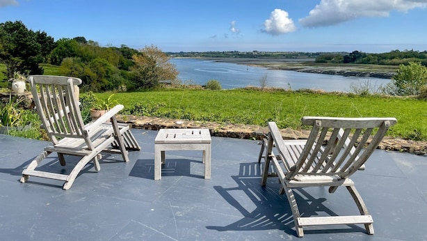 Een terras met houten stoelen en een tafeltje, met uitzicht op water en groen.