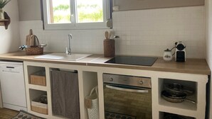 Een keuken met een raam, witte tegels, een spoelbak, een fornuis en kastjes.