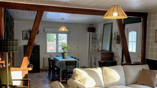 Een ruime woonkamer met een grote beige bank, een eettafel met stoelen, en een keuken op de achtergrond.