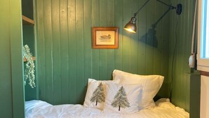 Een bed met witte beddengoed, twee kussens met boommotieven, een lijst met een foto aan de muur, en een klein houten tafeltje naast het bed.