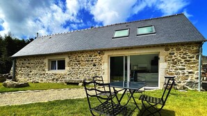 A stone house with a tiled roof, a glass door, and a patio with a table and chairs. - House Le Rohel (Pleubian)