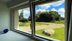 A room with two windows overlooking a garden with a table and chairs, a large rock, and a grassy area. - House Le Rohel (Pleubian)