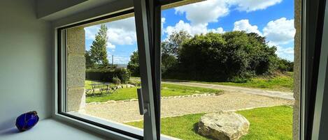 A room with two windows overlooking a garden with a table and chairs, a large rock, and a grassy area.