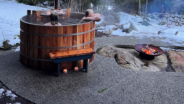 Un jacuzzi de madera con chimenea, rodeado de nieve y árboles.