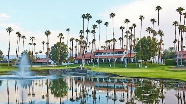 Un campo de golf con un estanque que refleja palmeras y un edificio de techo rojo.