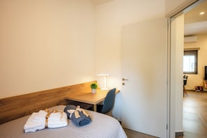 Ein Hotelzimmer mit einem Bett, einem Schreibtisch, einem Sessel, einer Lampe und einer Tür, die in einen anderen Raum führt.