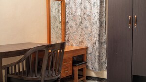 A wooden desk with a chair, a mirror, and a wardrobe in a room with patterned wallpaper. - Liwonde Park Motel (Liwonde)
