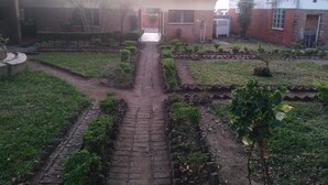 Ein Gartenweg führt zu einem Gebäude mit einem Ziegeldach, umgeben von Backsteinmauern und kleinen Bäumen.
