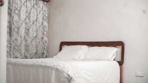 A bed with a wooden headboard in a room with plain walls and a patterned curtain. - Liwonde Park Motel (Liwonde)