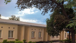 A building with a flat roof, multiple windows, and a garden area with various plants. - Liwonde Park Motel (Liwonde)