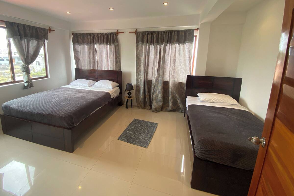 Quarto de hotel com duas camas, uma mesinha e uma janela com cortinas.