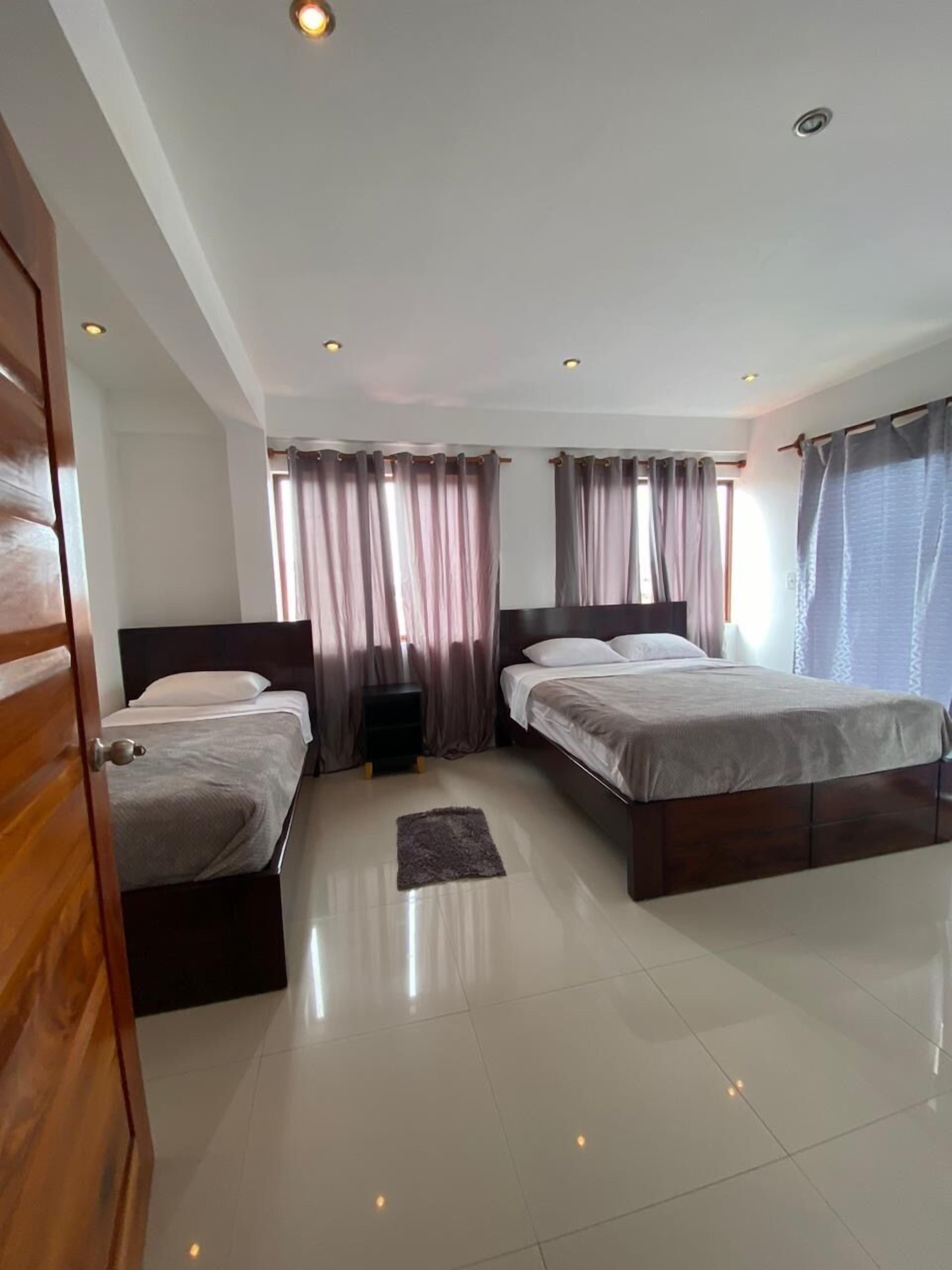 A modern hotel room with two beds, a wooden door, and a tiled floor.