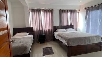 A modern hotel room with two beds, a wooden door, and a tiled floor.