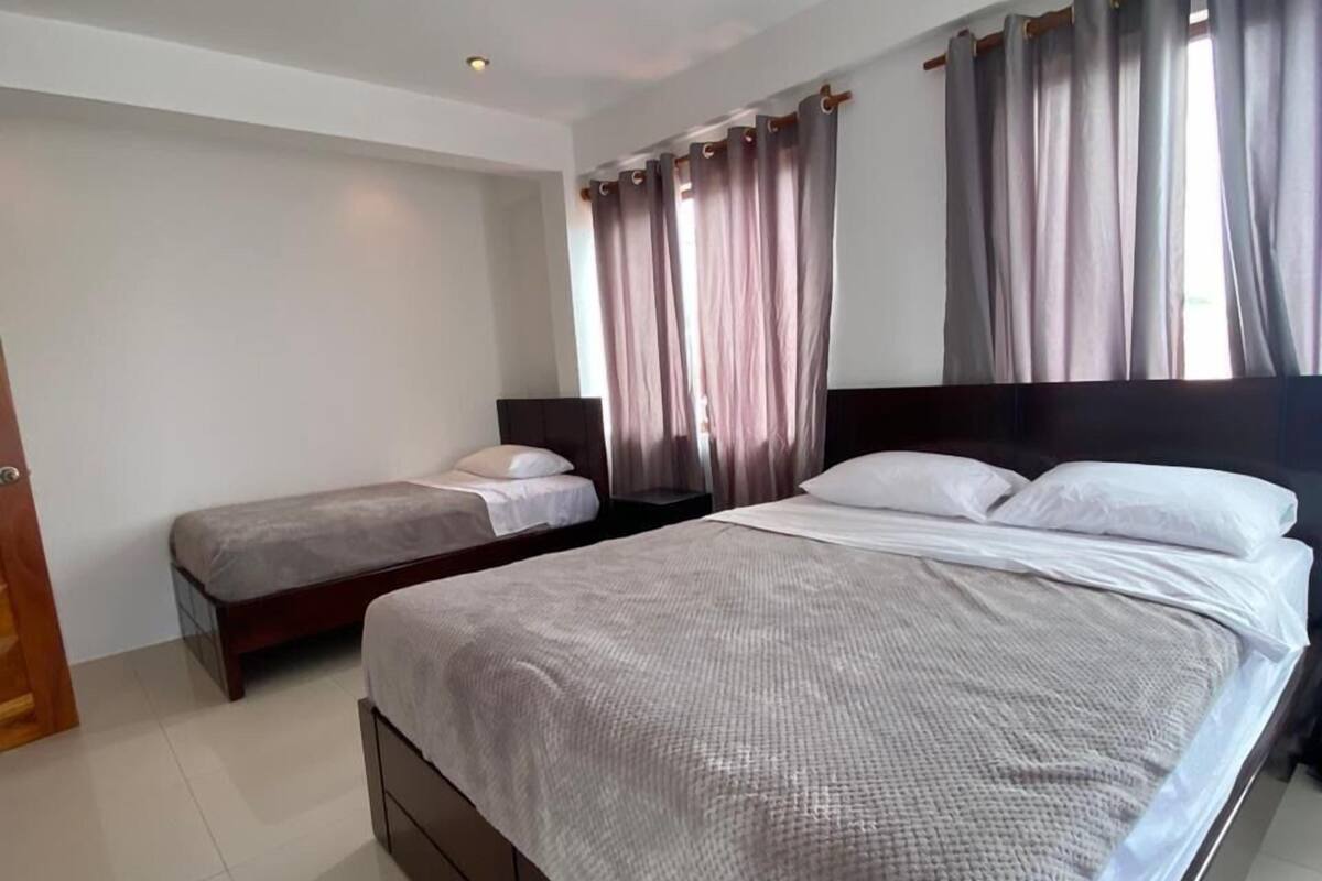 Quarto com uma cama grande, uma cama menor e uma mesa de cabeceira.
