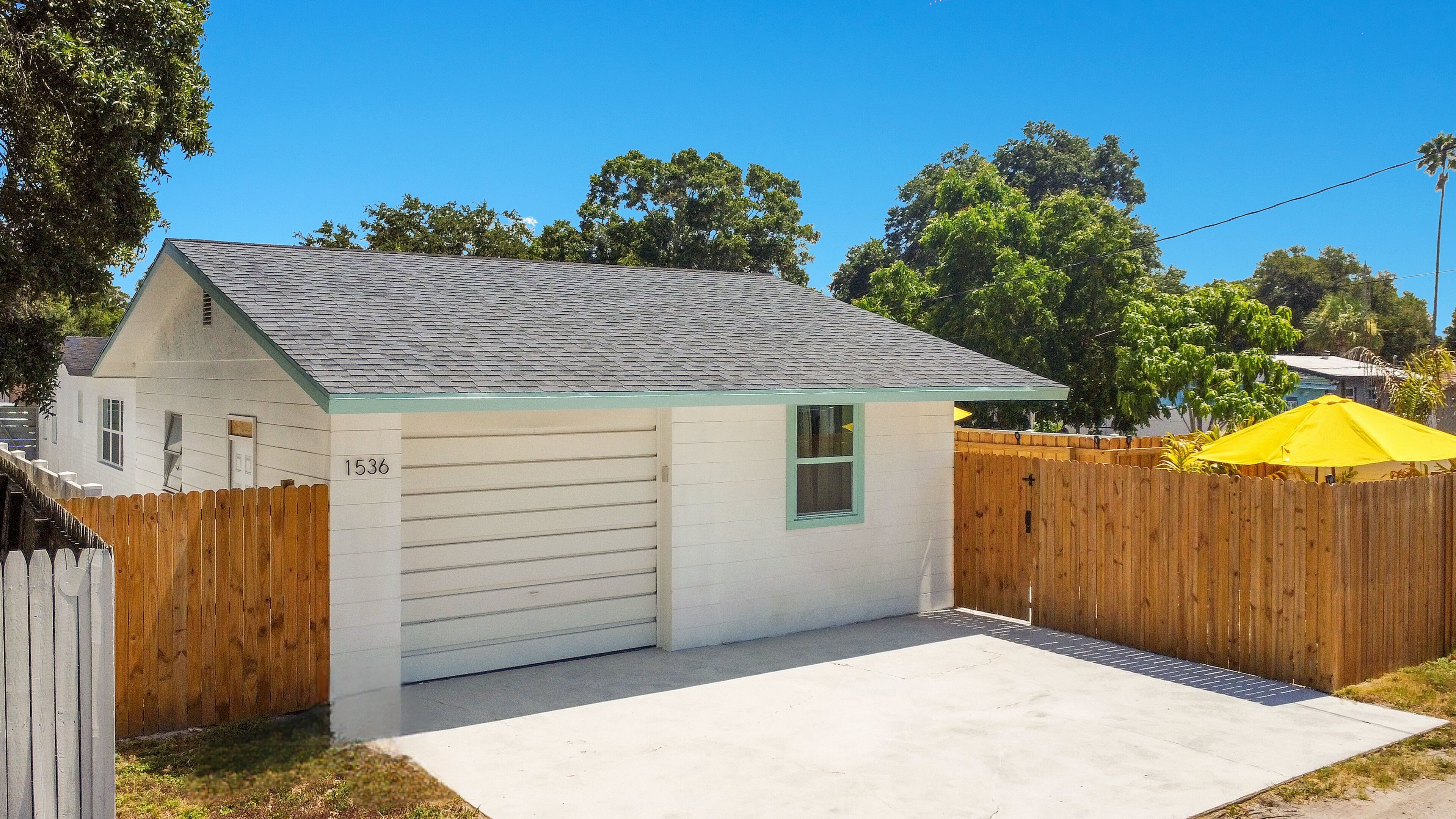 A small, single-story house with a garage, a wooden fence, and a yellow umbrella.