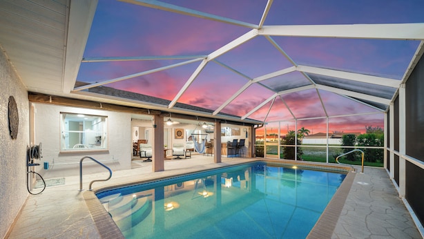 Ein Innenpool mit Blick auf den Sonnenuntergang durch eine Glasdecke, umgeben von Liegestühlen und einer Poolanlage.